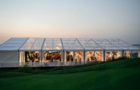 a wedding reception inside a clear tent at dusk