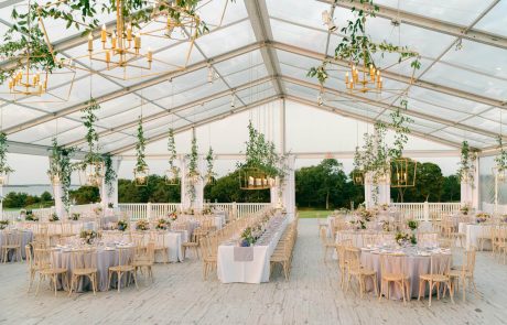 a beautiful clear tent on finished floor with chandeliers, tables and chairs